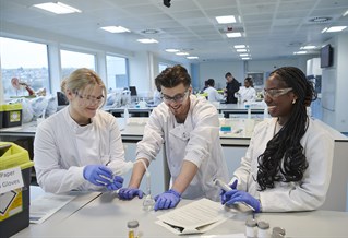 Three students in white lab coats doing experiments